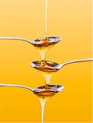 Syrup being poured into and overflowing from a set of consecutive spoons; demonstrates the high viscosity of syrup.