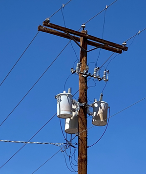 A picture of an electrical pole with 3 transformers (grey cylinder type structures) that take the 14kv power lines and step them down to 120 or 240 volts.