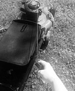 A photograph of a push mower with a hand ready to pull the start cord.